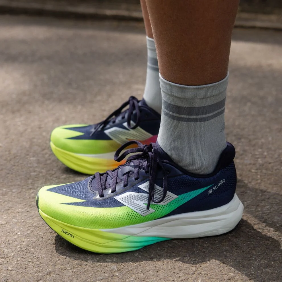 Two people posing indoors against a textured backdrop, wearing casual athletic outfits and sneakers. 